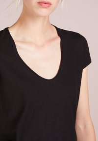 Schwarzes T-Shirt mit kurzen Ärmeln und tiefem V-Ausschnitt, aus weichem Stoff gefertigt, mit subtiler Textur und sauberer Naht an den Kanten.