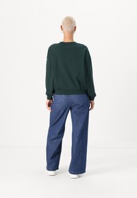 Sweat-shirt vert à manches longues avec un col rond, des épaules tombantes et un ourlet côtelé. Associé à un jean bleu décontracté et des baskets blanches.