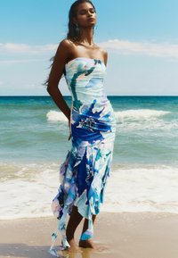 Robe maxi avec un motif floral coloré comprenant des nuances de bleu et de blanc ; design sans bretelles avec un corsage ajusté et un ourlet fluide.