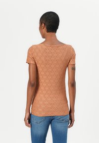Brunmønstrete strikket topp med korte ermer, med rund hals og teksturert design, kombinert med blå denimjeans.