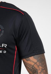 Zwarte sportshirt met rode accenten, korte mouwen en een gestructureerde stof. Bevat logo details aan de voorkant.