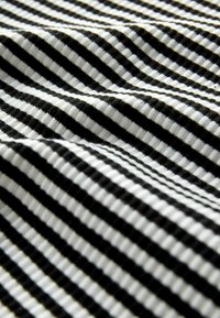 Bavlnená látka s striedajúcimi sa čiernymi a bielymi pásikmi, ktorá predvádza mäkký, texturovaný povrch s viditeľným rebrom v tkaní.