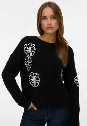 Pull en maille noire avec broderie florale blanche sur le devant et les manches. Doté d'un col rond et de manches longues et amples.
