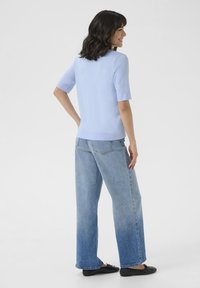 Pull léger bleu clair à manches courtes avec une coupe décontractée, associé à un jean large à taille haute en denim foncé et des chaussures plates noires.
