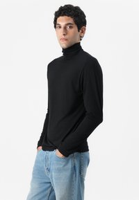 Fekete, testhezálló turtleneck felső, puha anyagból készült. Hosszú ujjú, magas nyakkivágással, világos kék farmernadrággal párosítva.