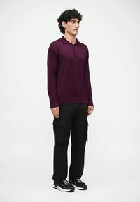 Bordo polo majica z dolgimi rokavi in dvema gumboma na sprednjem delu, kombinirana s črnimi cargo hlačami s stranskimi žepi in črnimi supergami.