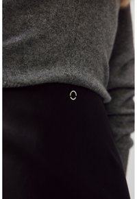 Harmaa neulepaita, joka on kerroksittain mustan hameen päällä, ja jossa on hopeinen ympyräkoriste vyötäröllä yksityiskohtana. Pehmeä pinta on näkyvissä.