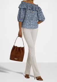 Modrá květinová blůza s odkrytými rameny a volánkovým výstřihem, doplněná bílými rozšířenými kalhotami a hnědou kabelkou ve tvaru kbelíku s detaily na zapínání.