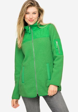 Veste en polaire verte avec une partie supérieure matelassée, poche zippée sur la manche et poches latérales. Tissu texturé et chaud.