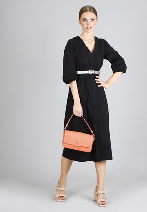 Black midi dress with puff sleeves, silver belt, and a textured coral handbag. Model wears beige block-heeled sandals. Simple backdrop.
