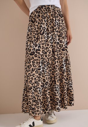 Jupe maxi à volants imprimée léopard avec taille élastique et cordon, portée avec des baskets blanches et un haut blanc partiellement visible.