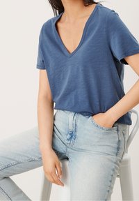 Modrá v-neck tričko vyrobené z měkké, lehké tkaniny, spárované s džínovými kalhotami světle modré barvy, s volným střihem a krátkým rukávem.