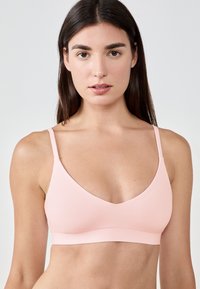 Bralette rose doux en tissu lisse, avec des bretelles réglables et un décolleté en V profond. Conception sans couture avec une large bande inférieure pour le soutien.