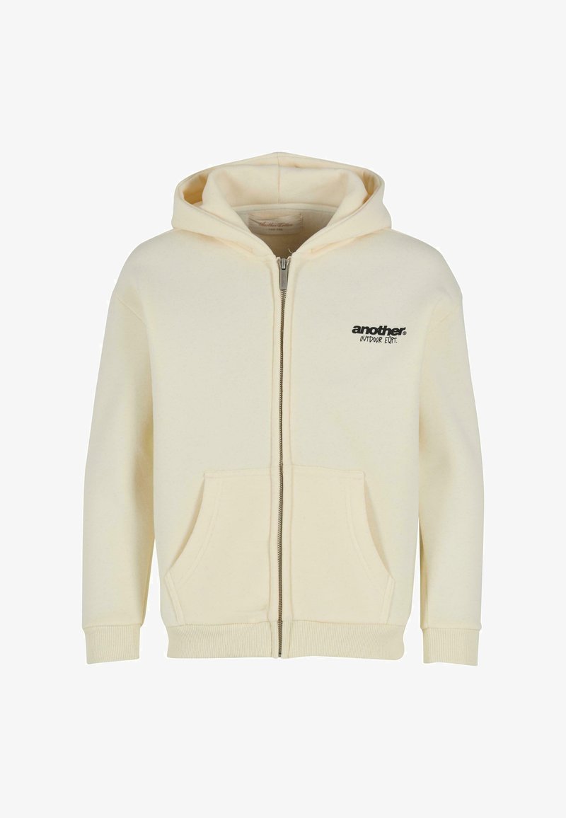 Crèmekleurige zip-up hoodie met een kangoeroezak, ribgebreide manchetten en een zwarte logoprint op de linkerkant van de borst. Zachte stof, casual ontwerp.