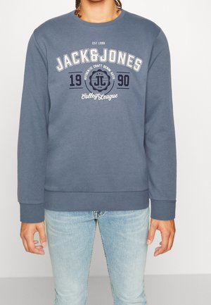 Felpa blu con colletto rotondo, maniche lunghe e polsini a coste. La parte anteriore presenta il logo "JACK & JONES" con testo e design circolare in colori contrastanti.