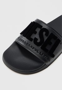 Mustad libisev sandaal laia rihmaga, millel on reljeefne, pehme logo tekstiga. Sile tald, mati viimistlusega ja ümarate servadega. Tekstuuriga jalapadi.