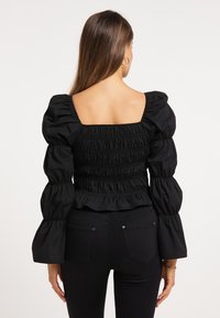 Sort smocket bluse med puffede ærmer og firkantet halsudskæring, der har en tætsiddende talje og flæse nederst. Glat, letvægtsstof.