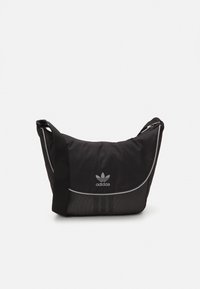 Borsa a spalla nera Adidas con forma curva, pannello laterale in rete, tre strisce bianche e tracolla regolabile. Tessuto testurizzato e dettaglio del logo.