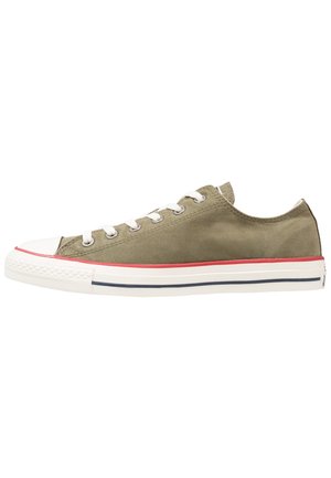 Matalavartinen oliivinvihreä kangastossu, jossa valkoinen kuminen kärki, valkoiset kengännauhat ja valkoinen pohja, jossa punaisia ja mustia raitoja.