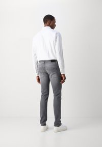 Jeans gris ajustados con bolsillos traseros, combinados con una camisa blanca de botones. El conjunto tiene una textura suave y líneas limpias, complementado con zapatillas blancas.