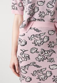 Gebreide roze top met korte mouwen en een bijpassende rok, voorzien van zwarte bloemmotieven en zakken aan de voorkant van de rok.