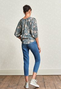 Top loose-fit a fiori blu e beige, abbinato a jeans azzurri alla caviglia e sneaker alte stampate.