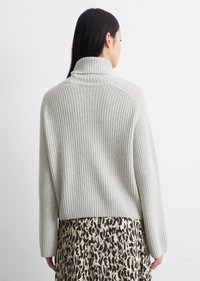 Lys grå ribbestrikket genser med høy krage og lange ermer, sammen med et mønstrete beige og brunt skjørt med leopardmønster.
