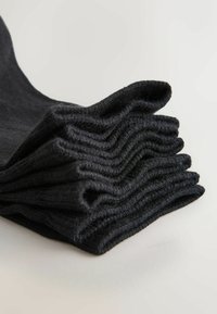 Pile de chaussettes noires en tricot côtelé pliées sur une surface claire avec une chaussette partiellement déployée.