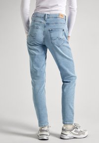Pantalones vaqueros de mezclilla azul claro con un corte ajustado, que cuentan con dos bolsillos traseros y un sutil diseño de costura en zigzag. Combinados con zapatillas grises.