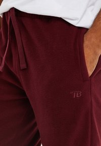Bordeaux fleece joggers met een elastische tailleband, zijzakken en een klein geborduurd logo op de linker bovenbeen. Zachte textuur en een ontspannen pasvorm.