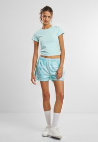 Lys blå tettsittende t-skjorte med korte ermer og en subtil logo. Kombinert med mønstrede lys blå shorts og hvite joggesko, kne-lange hvite sokker.