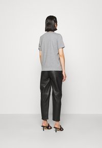 Grå kortærmet t-shirt parret med sorte læderbukser, der har en afslappet pasform og en glat tekstur. Sorte hælletter fuldender looket.
