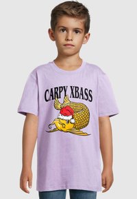 Lilac trumpas rankovėmis marškinėliai su geltonu animaciniu žuvimi, dėvinčia Kalėdų senelio skrybėlę, ir tekstu "CARPY XBASS" ryškiomis juodomis raidėmis.