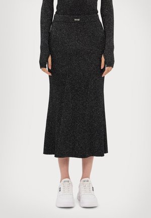 Schwarz gerippter Midi-Rock mit subtilen metallischen Fäden, ausgestelltem Saum und elastischem Bund. Kombiniert mit weißen Turnschuhen für einen lässigen Look.