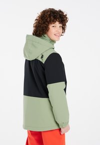 Veste colorée avec un haut vert clair, un bas noir et une capuche. Poignets et ourlet élastiques, tissu lisse avec un détail de logo.