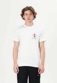 Hvid bomulds t-shirt med et lille brunt grafisk billede af en surfende hund og teksten "RIP CURL CALIFORNIA" i rødt. Klassisk crew neck design.