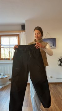 Schwarze Hose mit lockerem Schnitt, ausgestattet mit einem elastischen Bund, Seitentaschen und einer glatten Textur. Dezente Nähte sind sichtbar.