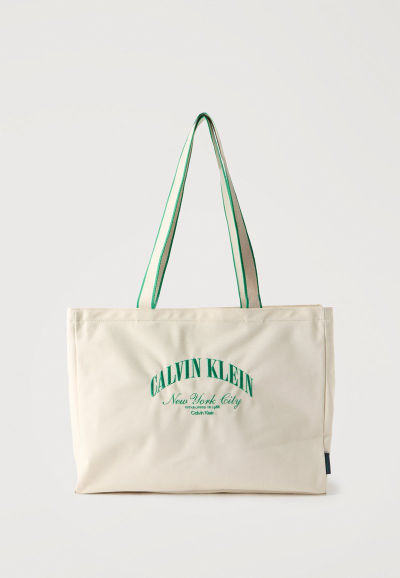 Sac cabas crème Calvin Klein avec texte vert et poignées assorties à rayures vertes sur fond blanc.