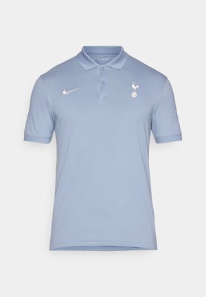 Polo de color azul claro con cuello, mangas cortas y un logo de Nike. Presenta un emblema de los Spurs en la zona del pecho izquierdo. Textura suave.