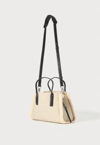 Beige taske med blødt, struktureret shearling-beslag. Har en struktureret form, sorte læderhåndtag og en justerbar skulderrem.