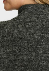 Maglione di lana grigio scuro con un collo alto. La texture appare pelosa e morbida, mostrando una miscela di fibre scure e chiare in tutto il tessuto.