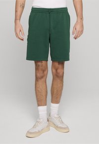 Groene shorts van een katoenmengsel met een elastische tailleband, trekkoorden, zijzakken en een klein logodetail aan de zoom. Gecombineerd met witte sneakers.