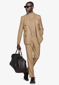 Tan dobbeltrækket jakkeset med matchende turtleneck, brun læder duffel taske og mørkebrun dress sko med snørebåndsdetalje.