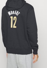 Felpa nera in misto cotone con orlo a coste grigio, con la scritta "MORANT" e il numero "12" stampati in bianco e oro sul retro.