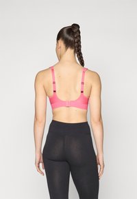 Rosa treningstopp med justerbare stropper, krokfeste og teksturert design. Kombinert med høyt liv svarte leggings.