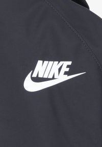 Čierna bunda s hladkým povrchom so zreteľným bielym logom Nike na ľavej hrudnej časti. Navrhnutá s minimálnymi švami.