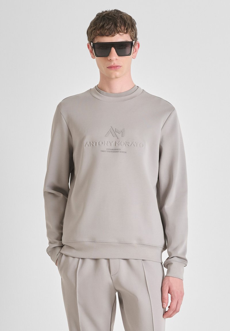 Sudadera gris de manga larga, cuello redondo, logo en relieve en el pecho, textura suave, combinada con pantalones ajustados a juego.