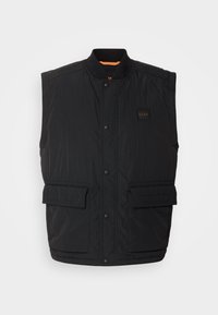 Veste matelassée noire sans manches avec boutons-pression, deux poches avant à rabat et un petit écusson carré avec logo sur la poitrine.
