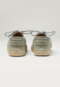 Espadrilles en daim gris avec un dos arrondi, des lacets ronds et des semelles en jute. Présente des coutures le long de la semelle et des œillets en métal pour les lacets.