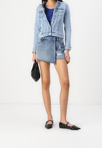 Ljusblå denimjacka med en åtsittande design, matchad med en slitna denimminikjol. Accessoarer i form av en svart handväska och platta skor.